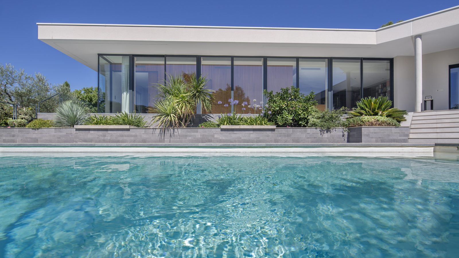 Villa contemporaine vue depuis la piscine, baies coulissantes aluminium sur toute la longueur de la façade