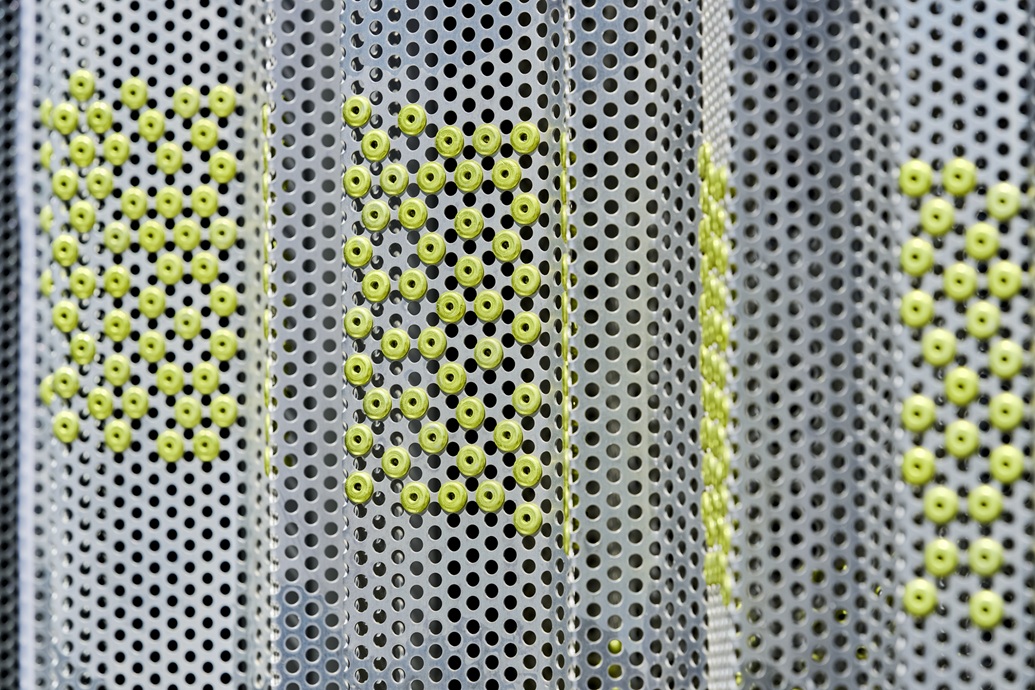 Gros plan sur les rivets en aluminium jaune citron posés dans la tôle perforée de la façade