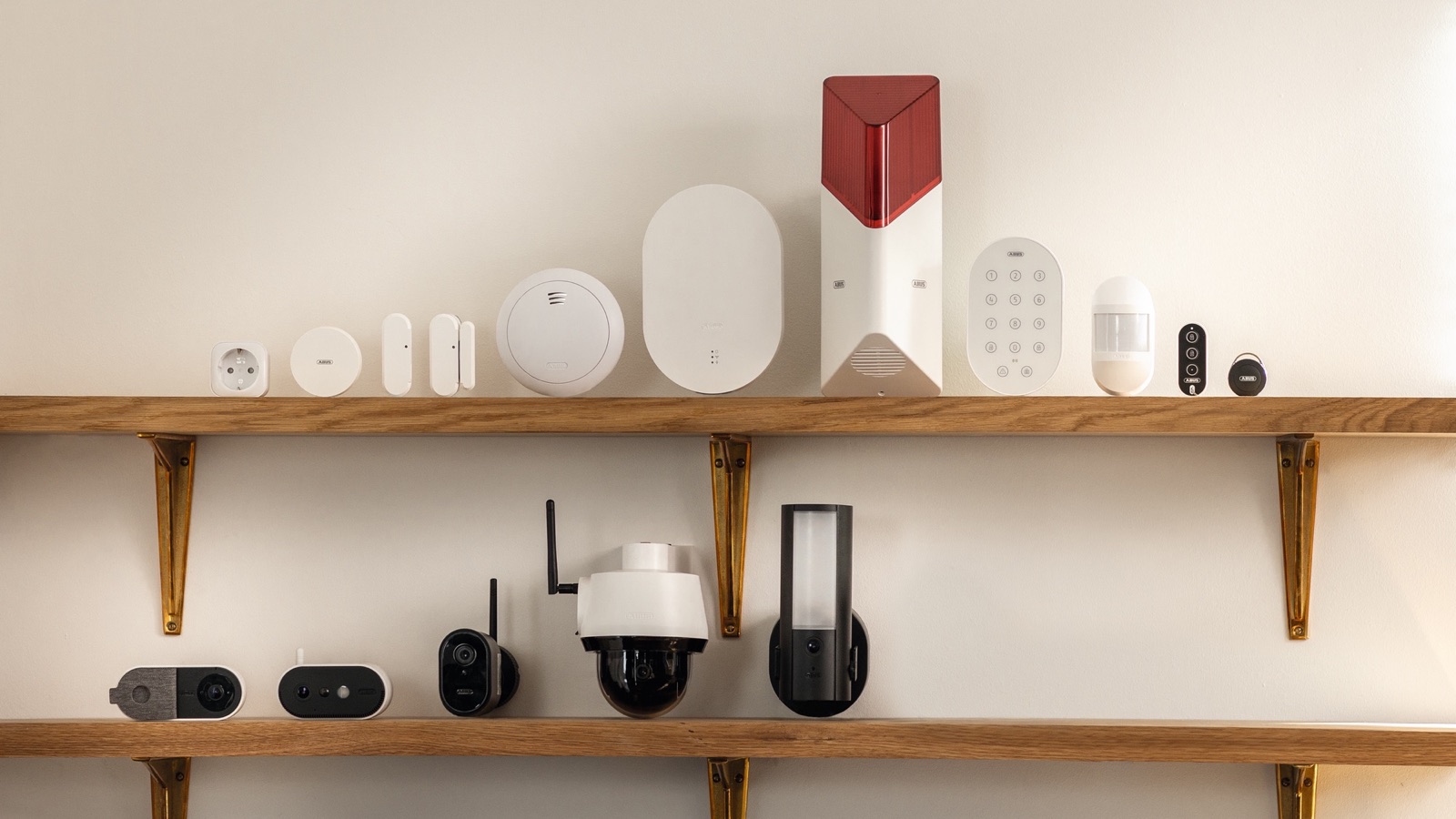 Détecteurs, sirène, clavier et caméras de la gamme ABUS Smartvest Pro alignés sur deux étagères en bois