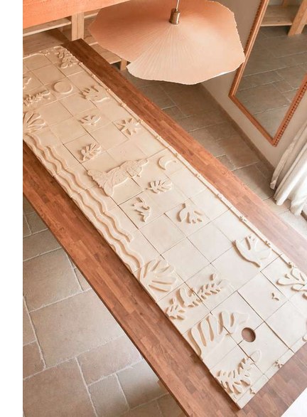 Fresque murale en céramique posée à plat sur un banc, ses carreaux assemblés en une longue bande à motifs