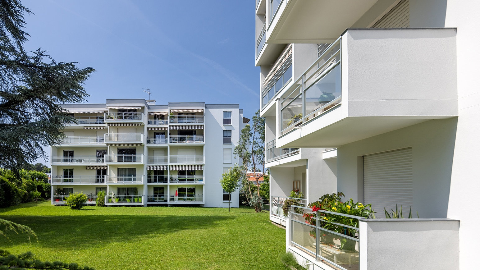 Résidence collective blanche après isolation par l’extérieur, balcons et pelouse au premier plan