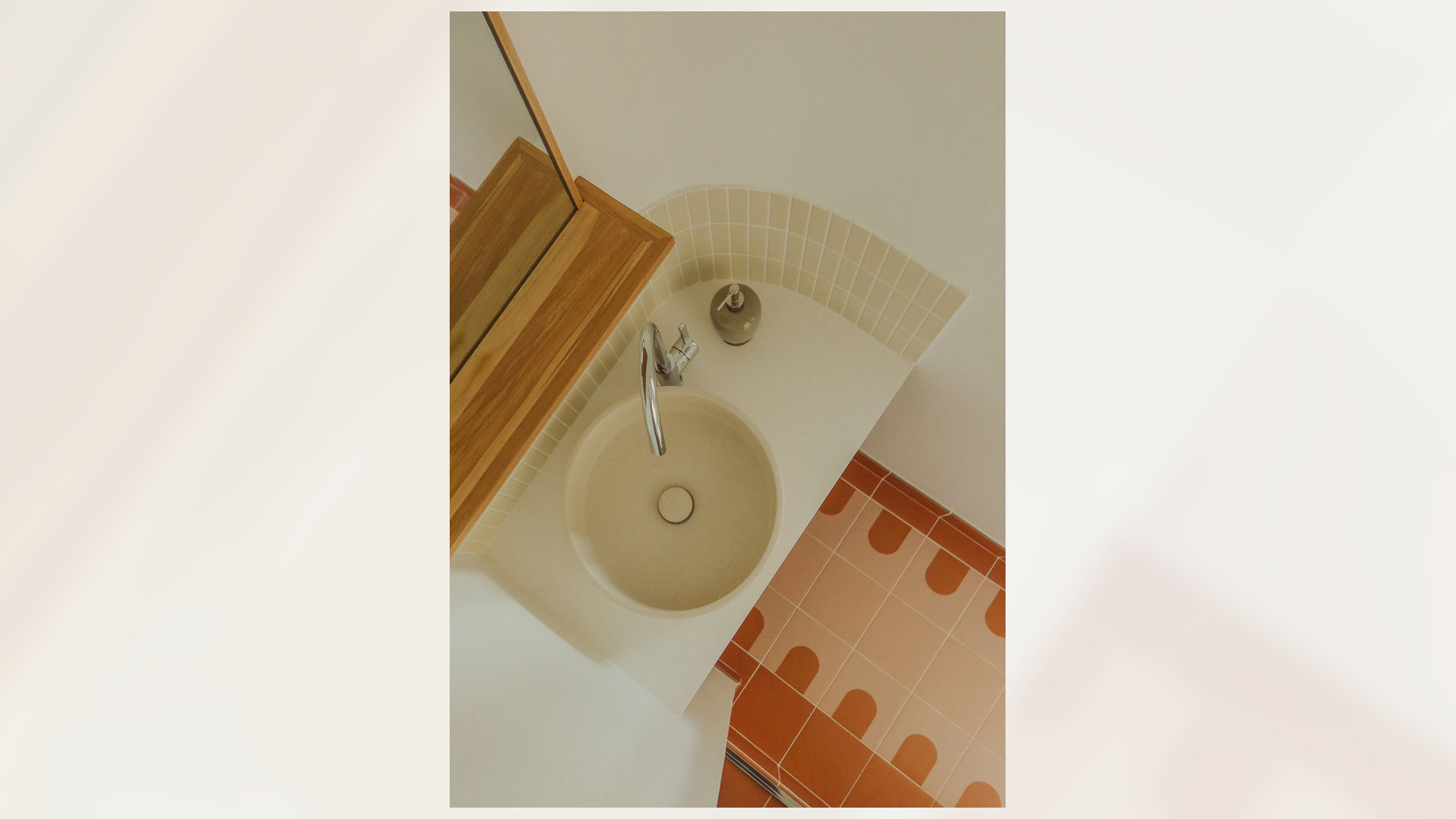 Vasque ronde crème vue de dessus, sol en terre cuite à motifs orangés et plan de toilette en bois clair