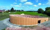 Bâtiment circulaire en bois-paille du Domaine Nebout avec façade courbe et toit incliné.