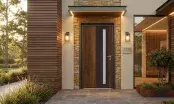 Porte d'entrée monobloc à parement bois sur une façade contemporaine en pierre et bardage bois, éclairée au crépuscule.