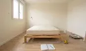 Chambre d'un logement en rénovation avec un lit deux places, mètre à ruban déroulé au sol le long du couchage