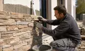 Poseur appliquant une plaquette de pierre naturelle sur un mur encollé au peigne, niveau à bulle en appui