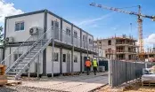 Base vie de chantier sur deux niveaux avec escalier et coursive, grue et bâtiment en construction en fond