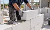 Maçon posant un bloc de béton cellulaire blanc sur un lit de mortier-colle appliqué en joint mince