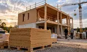 Chantier d'ossature bois en fin de gros œuvre, panneaux d'isolant biosourcé empilés sur palette au premier plan
