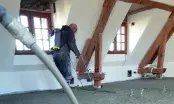 Chapiste réglant une chape fraîchement pompée dans un comble aménagé, le tuyau de pompe traversant la pièce