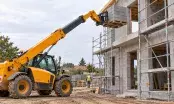 Chariot télescopique jaune déposant une palette de parpaings au plancher d'étage d'une maison en blocs béton