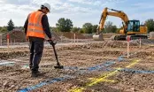 Technicien en gilet orange utilisant un détecteur de réseaux sur un terrain marqué au sol avant terrassement