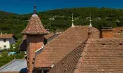 Toiture en tuiles terre cuite rouges avec un épi de faîtage conique et des cheminées, village en arrière-plan.