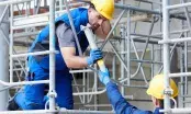 Deux ouvriers portant des gants de protection bleus assemblent les tubes métalliques d'un échafaudage de chantier