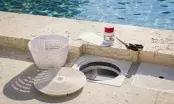 Skimmer de piscine ouvert au bord du bassin, avec son panier, le flacon de réparation et le tissu de renfort