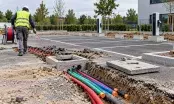 Tranchée ouverte sur un parking, fourreaux de couleurs posés devant une chambre de tirage béton