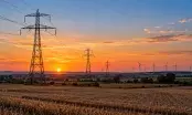 Ligne électrique haute tension traversant une plaine au crépuscule, éoliennes visibles à l'arrière-plan