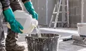 Mains gantées d’un ouvrier versant une résine depuis un bidon de chantier dans un seau de gâchage