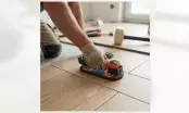 Carreleur agenouillé manipulant un carreau imitation bois avec une ventouse électrique posée à plat