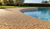 Plage de piscine en moquette de pierre, surface granuleuse continue épousant la courbe du bassin