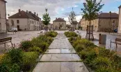 Place de village après la pluie, cheminement en dalles de pierre bordé de noues plantées de graminées