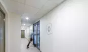 Couloir d'immeuble de logements équipé d'un plafond modulaire à dalles blanches, avec ascenseur et une personne qui passe.