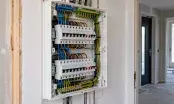 Tableau électrique ouvert dans un logement en rénovation, deux rangées de disjoncteurs et conducteurs repérés