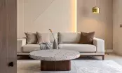 Table basse ronde dont le plateau en terrazzo clair laisse voir des éclats de bois de vigne, dans un salon beige