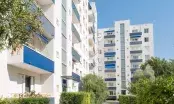 Façade blanche et bleue d'une résidence de logements collectifs après ravalement, balcons et végétation