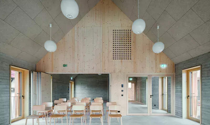 Salle polyvalente à charpente apparente dont le plafond en pente est habillé de dalles acoustiques en laine de bois.