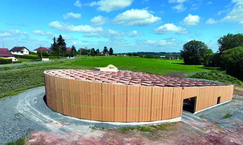 Bâtiment circulaire en bois-paille du Domaine Nebout avec façade courbe et toit incliné.