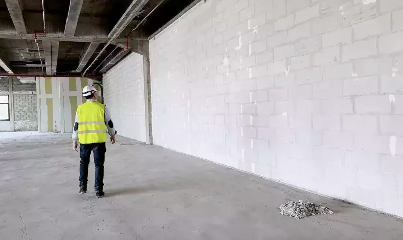 Chantier avec un mur en blocs de béton cellulaire blanc et un ouvrier en tenue de sécurité.