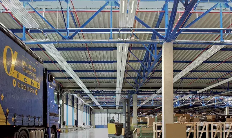 Plafond de hall industriel équipé de panneaux rayonnants et de luminaires linéaires intégrés, vu en contre-plongée.