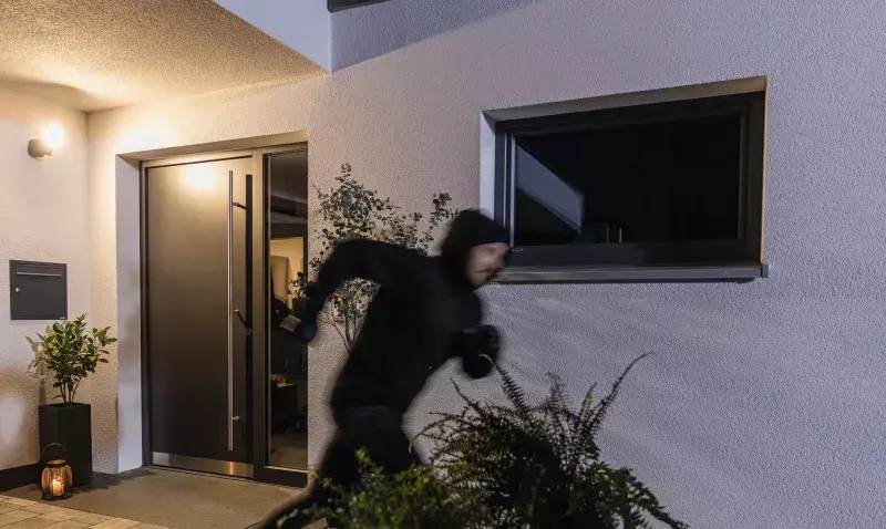 Silhouette encapuchonnée s'enfuyant de nuit devant la fenêtre oscillo-battante entrouverte d'une maison