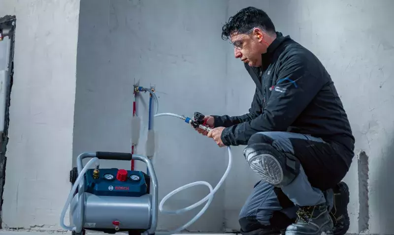Technicien raccordant un flexible au compresseur Bosch GKO18V-51 pour un test de pression sur un réseau d'eau