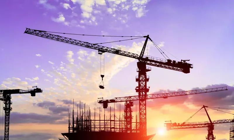 Chantiers de construction ralentis, grues immobiles sous un ciel nuageux, signe d'incertitude