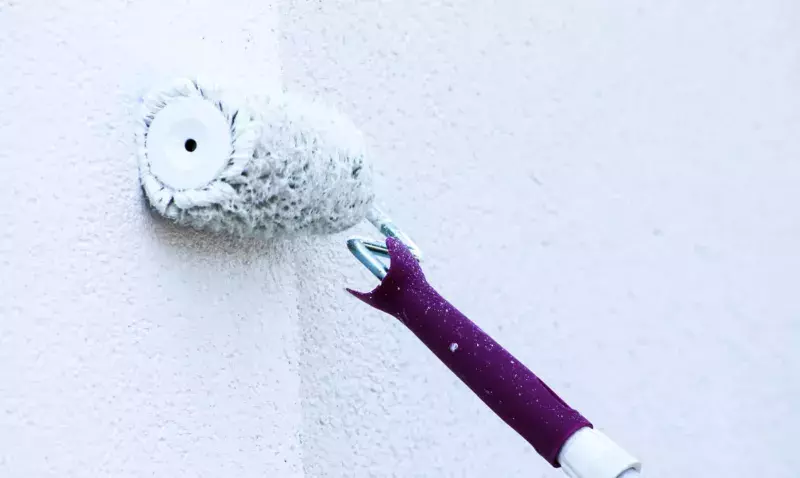 Rouleau appliquant une peinture blanche sur un mur de façade au grain marqué, en cours de ravalement