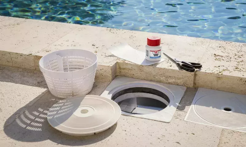 Skimmer de piscine ouvert au bord du bassin, avec son panier, le flacon de réparation et le tissu de renfort
