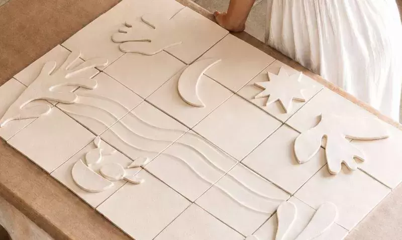 Fresque murale en céramique claire composée de carreaux à motifs en relief, posée à plat sur un établi