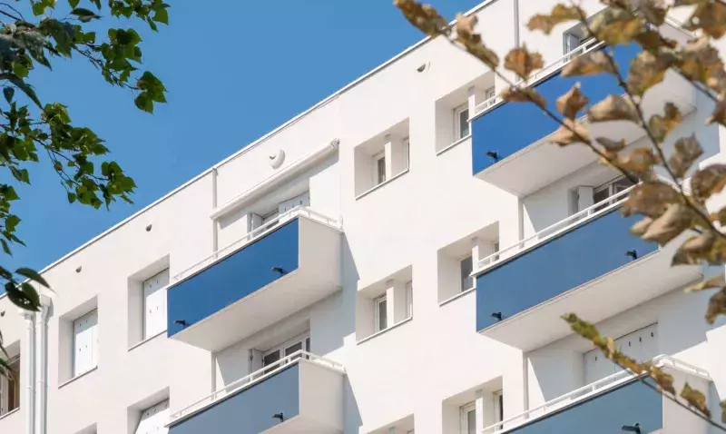 Façade d'un immeuble isolé par l'extérieur après finition, balcons bleus et enduit clair sous un ciel dégagé