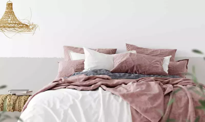 Chambre aux murs clairs peints avec du linge de lit rose poudré, suspension en rotin et plantes vertes