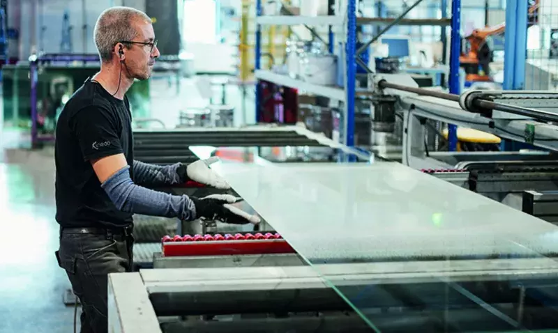 Un opérateur guide une grande plaque de verre sur la ligne de production d'un atelier industriel