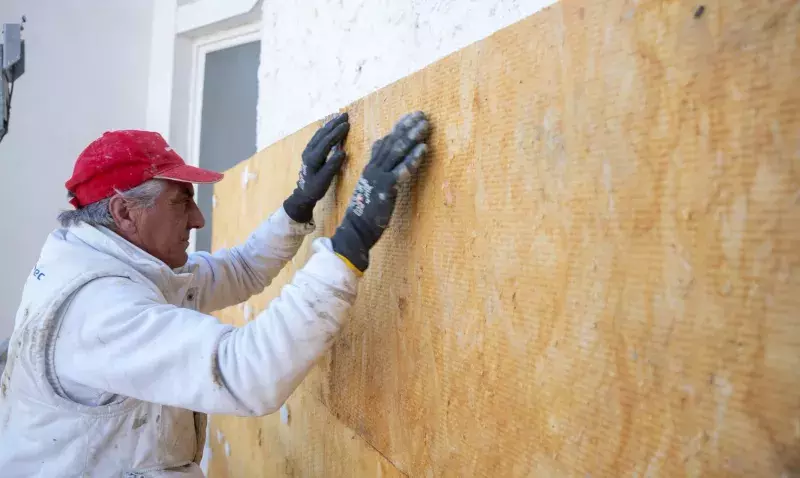 Applicateur plaquant un panneau de laine de verre sur une façade, plots de colle blancs visibles