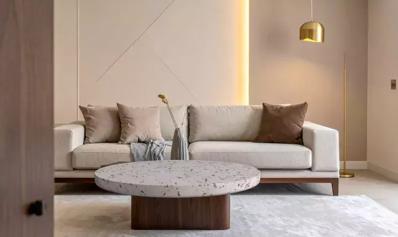 Table basse ronde dont le plateau en terrazzo clair laisse voir des éclats de bois de vigne, dans un salon beige