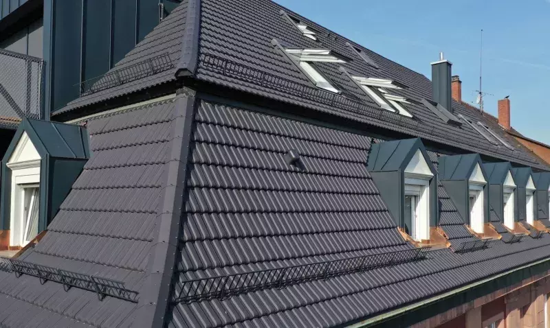 Toiture urbaine en tuiles terre cuite anthracite, avec chiens-assis en zinc, fenêtres de toit et arrêts de neige.