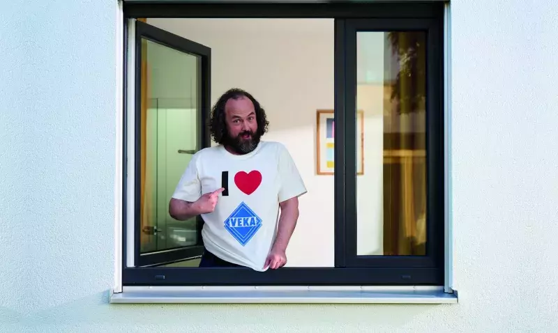 Hugo, personnage de la campagne VEKA, accoudé à une fenêtre PVC ouverte et désignant son t-shirt I love VEKA