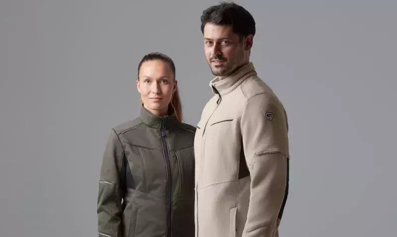 Deux professionnels en veste de travail beige et kaki, debout côte à côte sur fond gris uni en studio.
