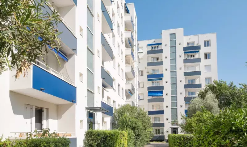 Façade blanche et bleue d'une résidence de logements collectifs après ravalement, balcons et végétation